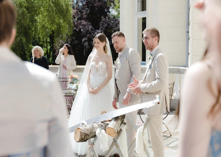 Brautpaar beim traditionellen Baumstammsägen auf der Schlossterrasse des Eventschloss Schönfeld