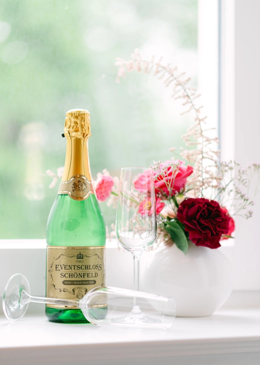 Sektflasche des Eventschloss Schönfeld mit Gläsern und Blumendekoration